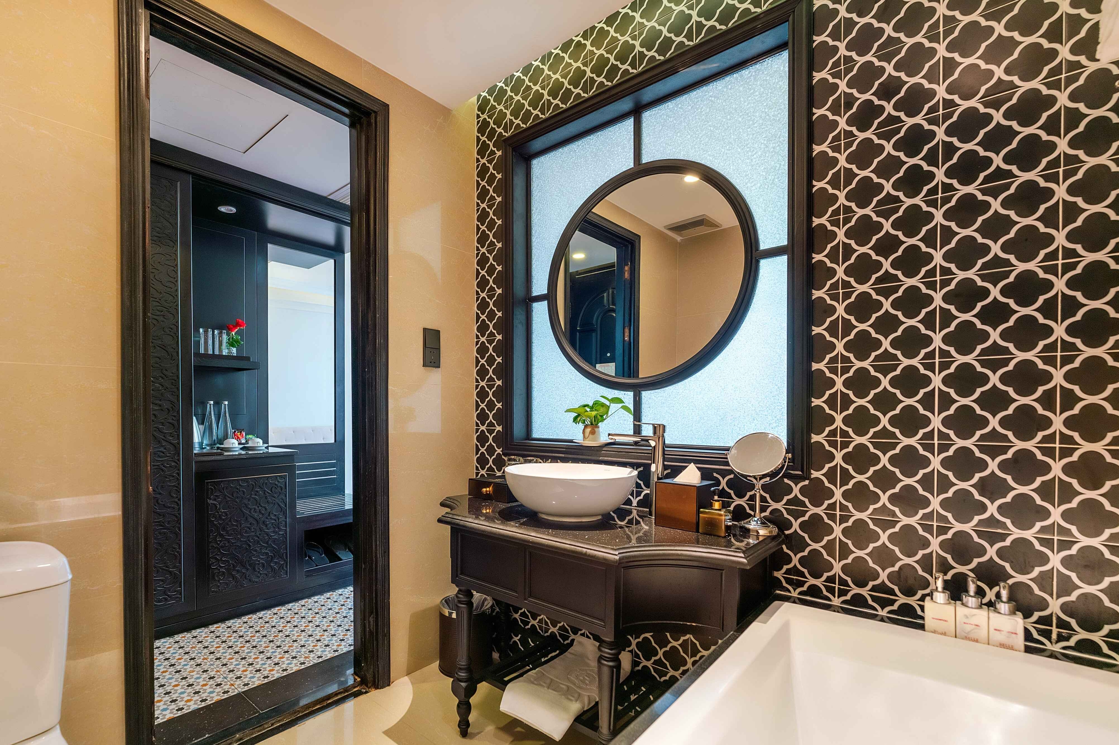 Stylish bathroom with a modern sink, decorative mirror, and patterned tiles, featuring a view of the adjoining area