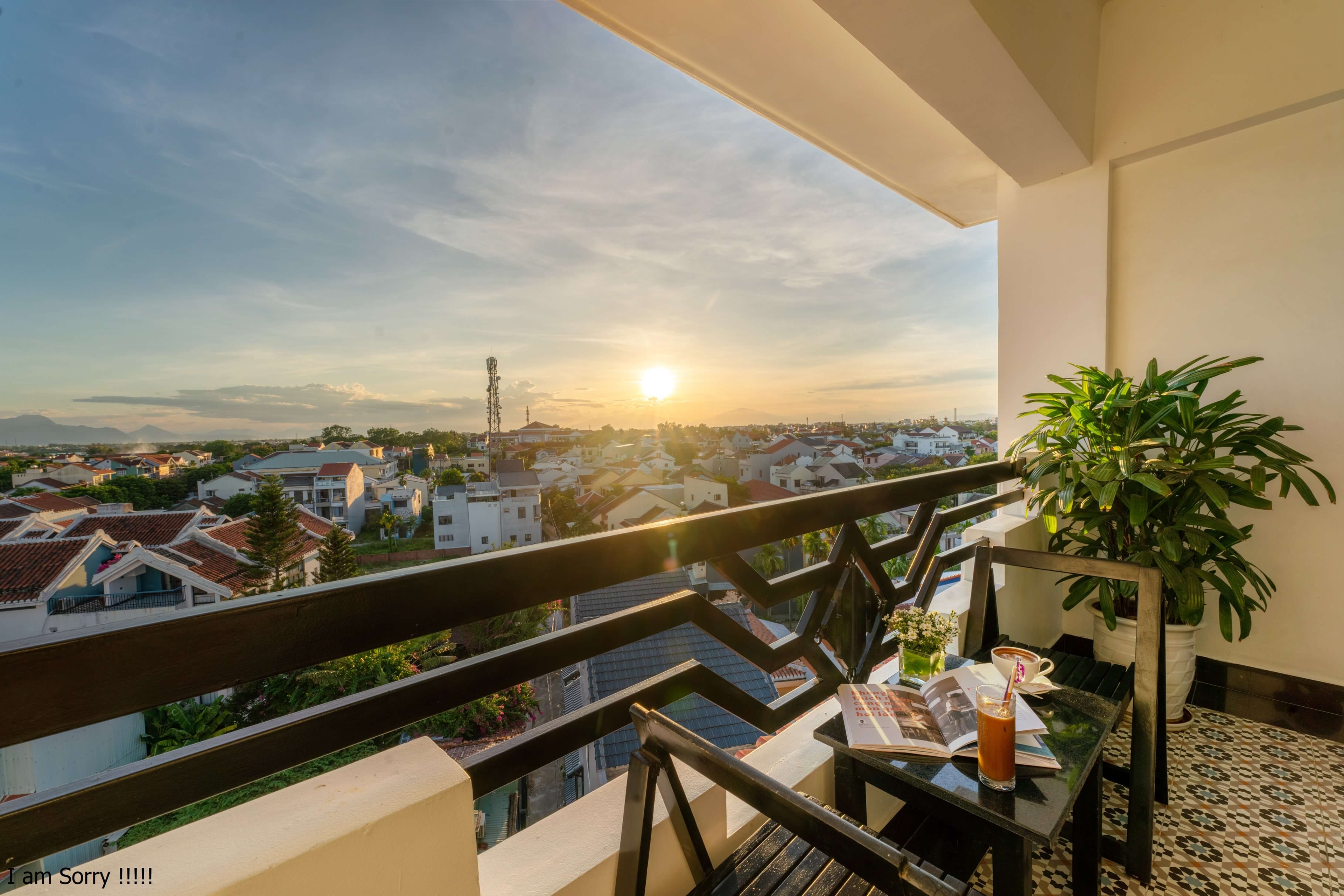 Balcony view at sunset, featuring a table with refreshments and a potted plant, overlooking a scenic landscape