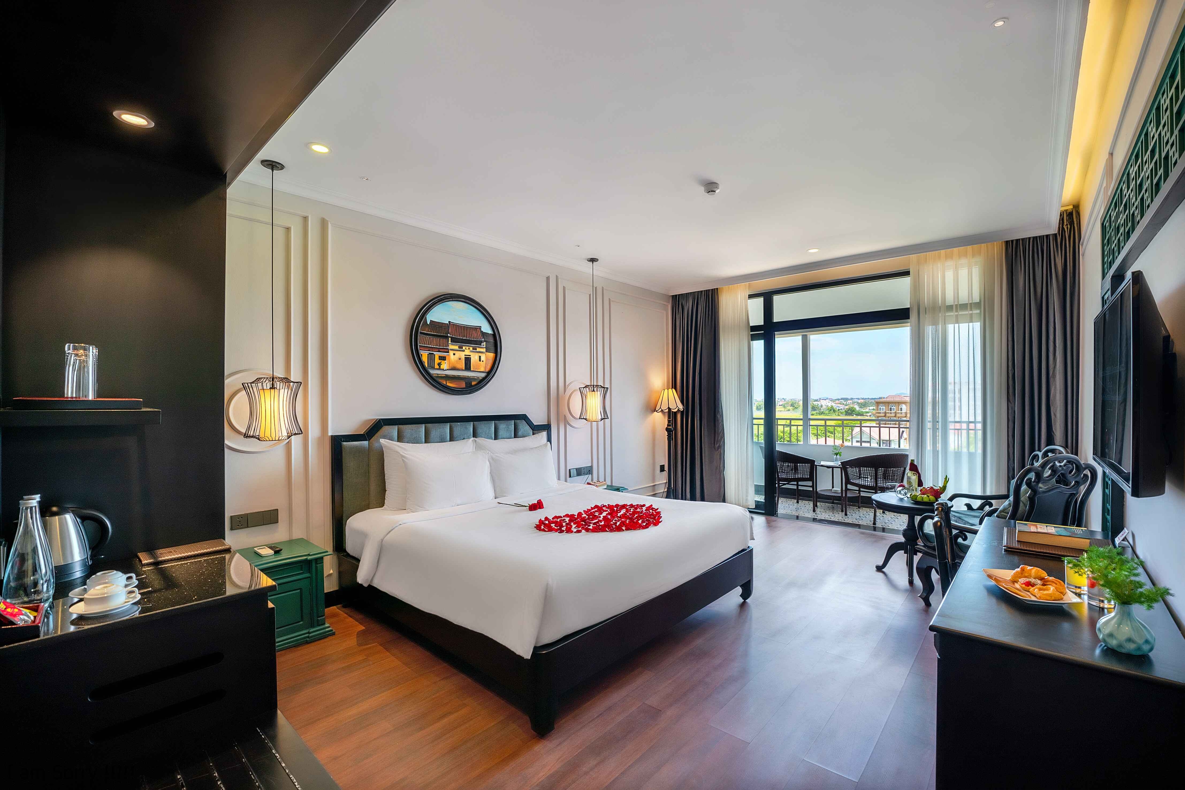 Modern hotel room featuring a queen-sized bed, wooden flooring, and large windows offering a view of the outdoors. The room includes a seating area and a desk with amenities, creating a welcoming and spacious environment