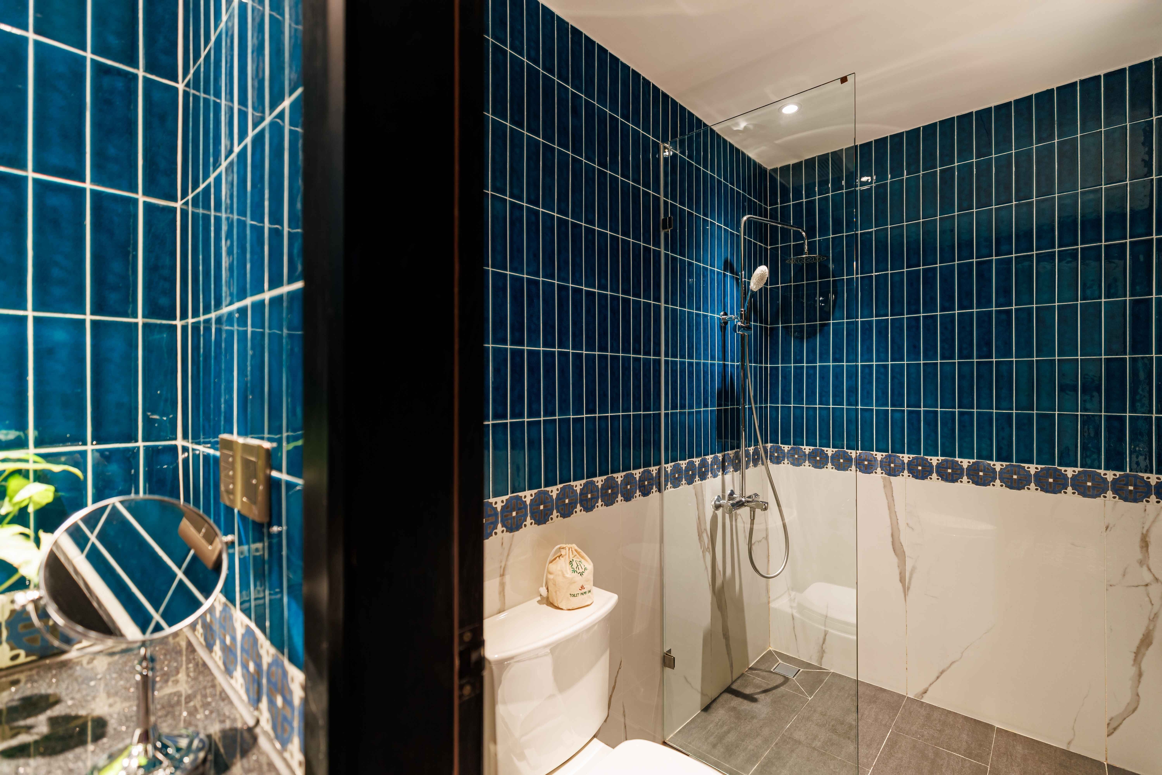 Vibrant bathroom featuring striking blue tiled walls and a modern shower area. A white toilet is visible, along with a sleek sink and mirror. The combination of colors creates a fresh and lively atmosphere, enhancing the overall design of the space