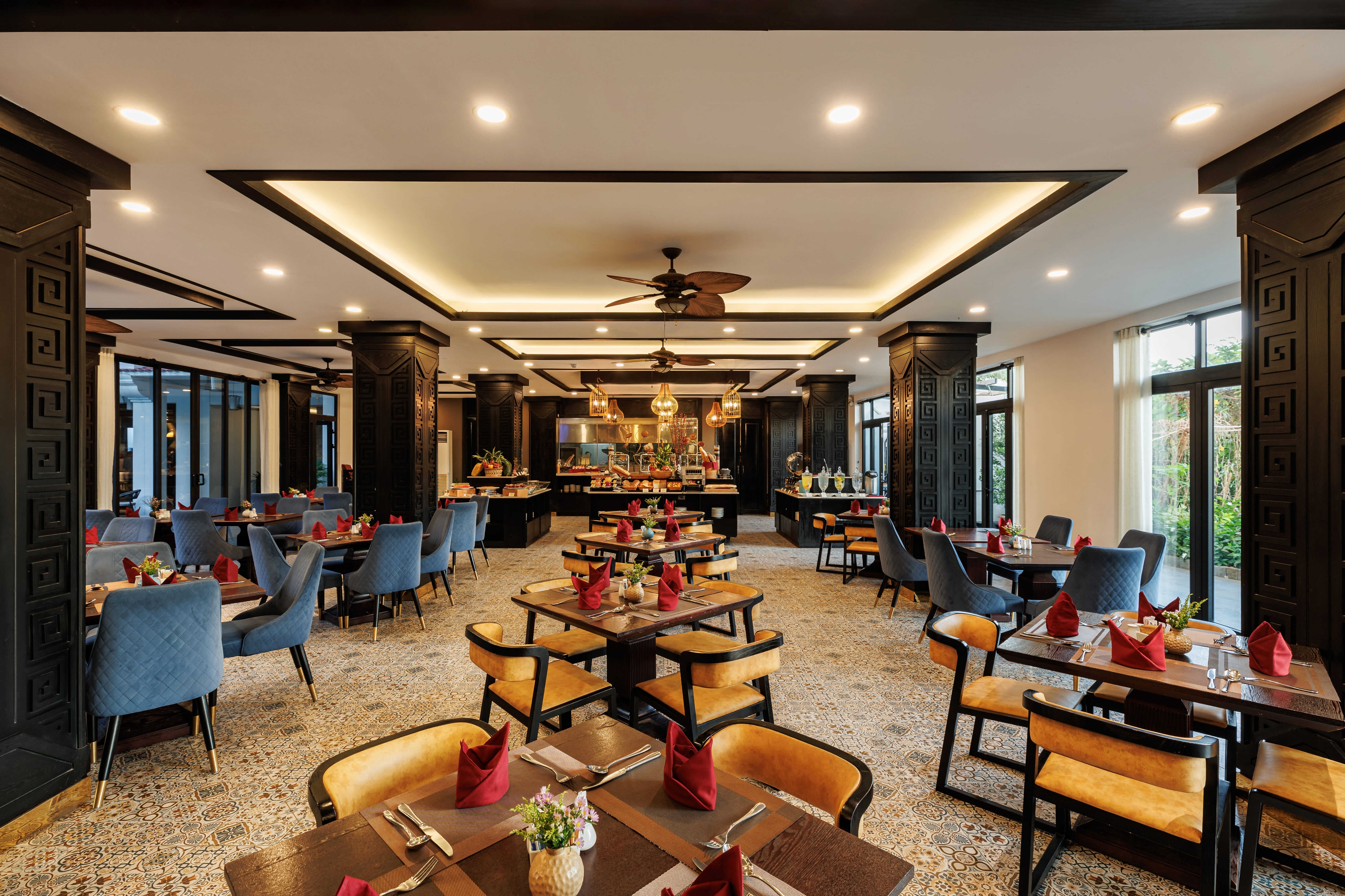 Interior view of a stylish restaurant featuring neatly arranged tables with wooden chairs and blue upholstered seating. The space is well-lit with modern lighting fixtures enhancing the elegant atmosphere.