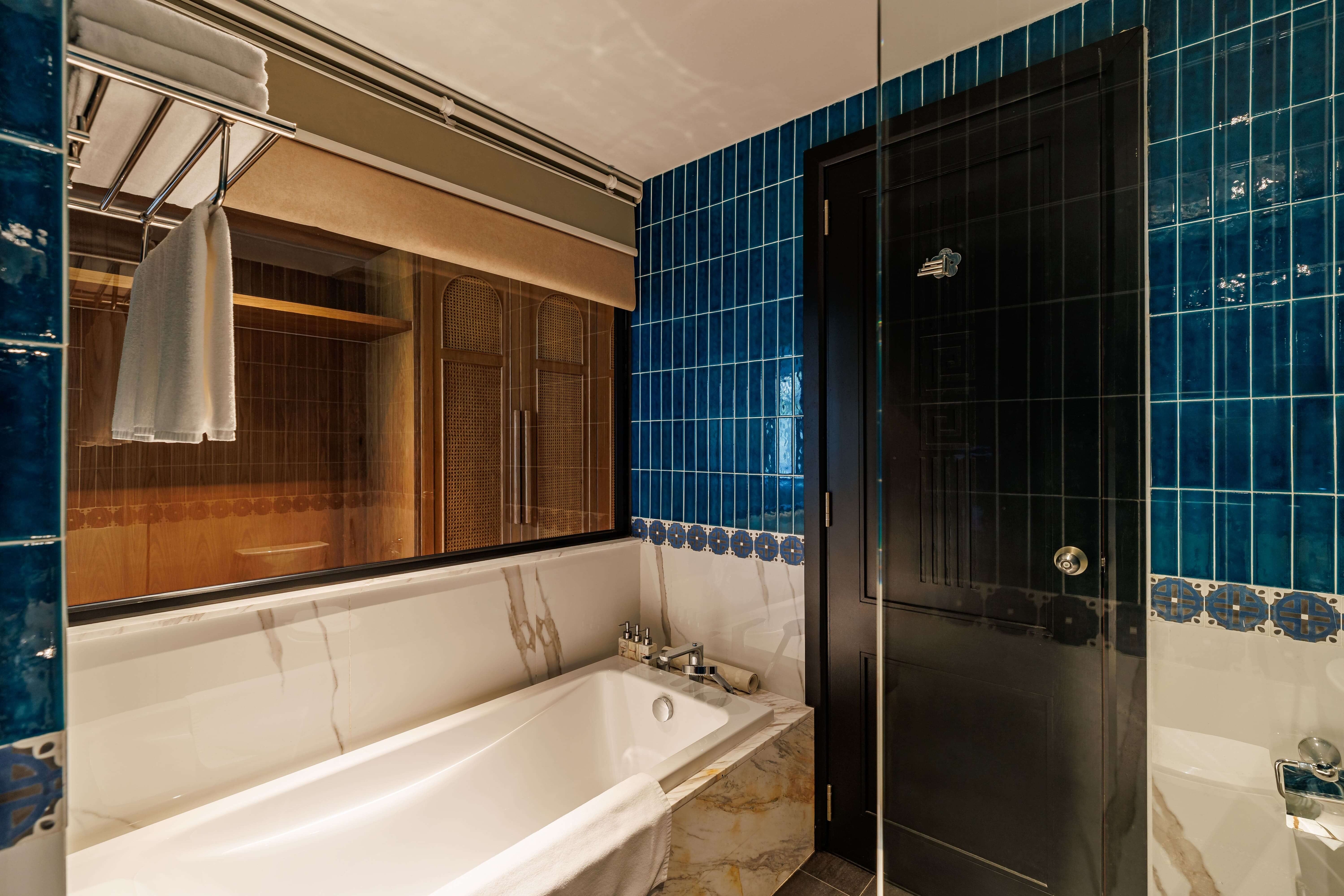 Stylish bathroom featuring a modern bathtub and a separate shower area. The walls are adorned with vibrant blue tiles, creating a striking visual contrast. A large window allows natural light to illuminate the space, while sleek fixtures add a contemporary touch