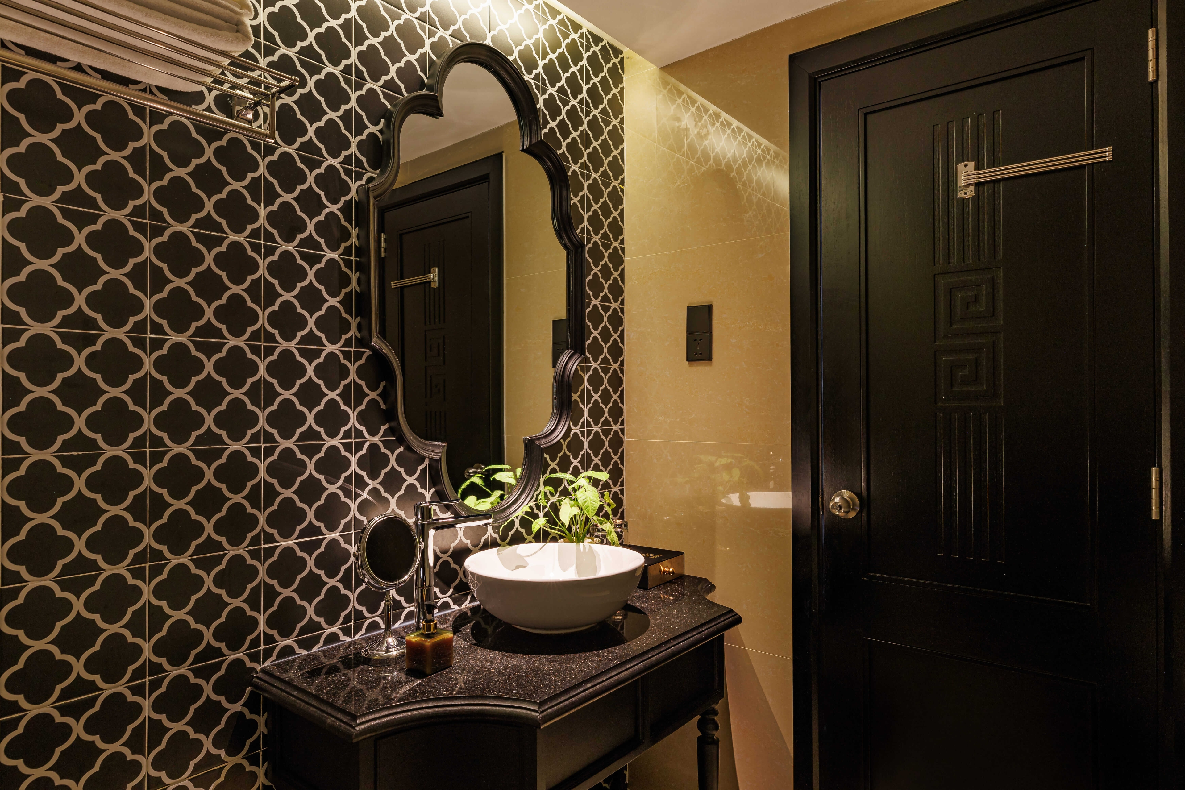 Elegant bathroom featuring patterned tiles on the wall, a stylish sink on a dark wooden vanity, and a large mirror with a decorative frame. Soft lighting creates a warm ambiance, enhancing the sophisticated décor
