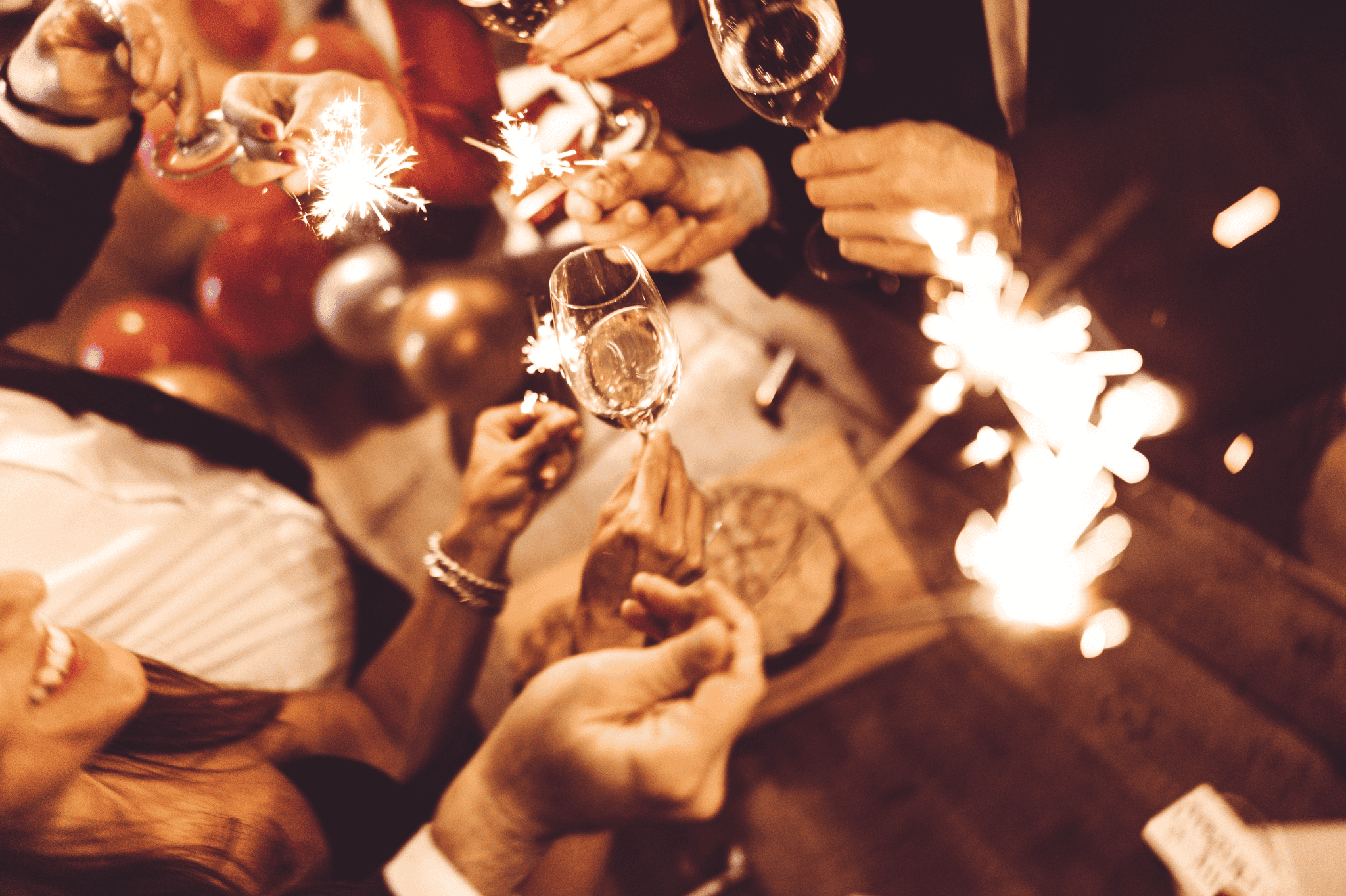 Celebrate with glasses of champagne, surrounded by festive decorations and sparklers. The atmosphere is celebratory, with balloons in the background creating a joyful ambiance.