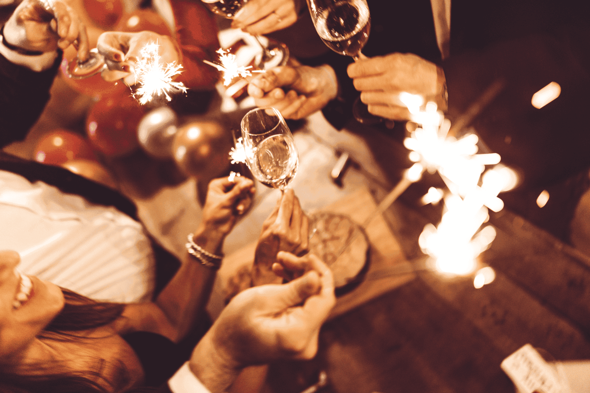Celebrate with glasses of champagne, surrounded by festive decorations and sparklers. The atmosphere is celebratory, with balloons in the background creating a joyful ambiance.